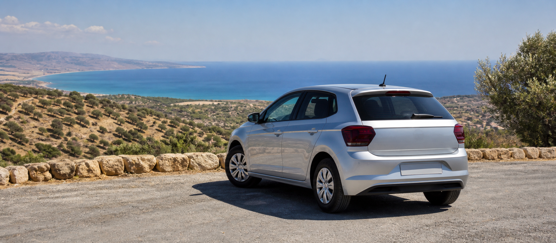 An unbranded silver hatchback parked at a Cyprus coastal viewpoint above olive-covered hills and the Mediterranean
