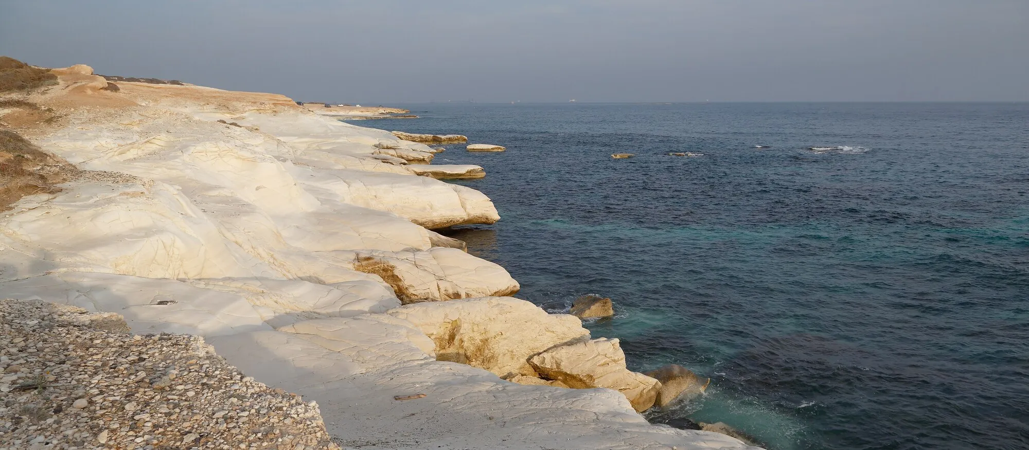 White chalk rock shelves running down to a blue-green sea at Governor's Beach on the south coast of Cyprus, in soft evening light