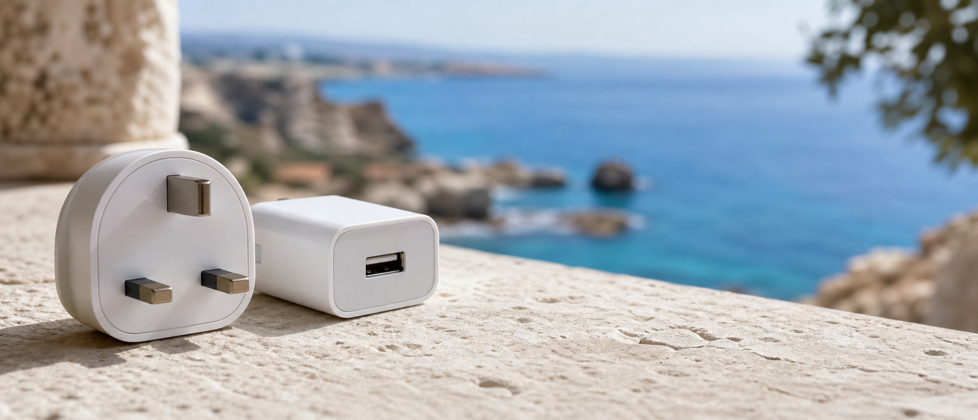 A white British Type G plug and USB charger on pale Cyprus stone beside the Mediterranean