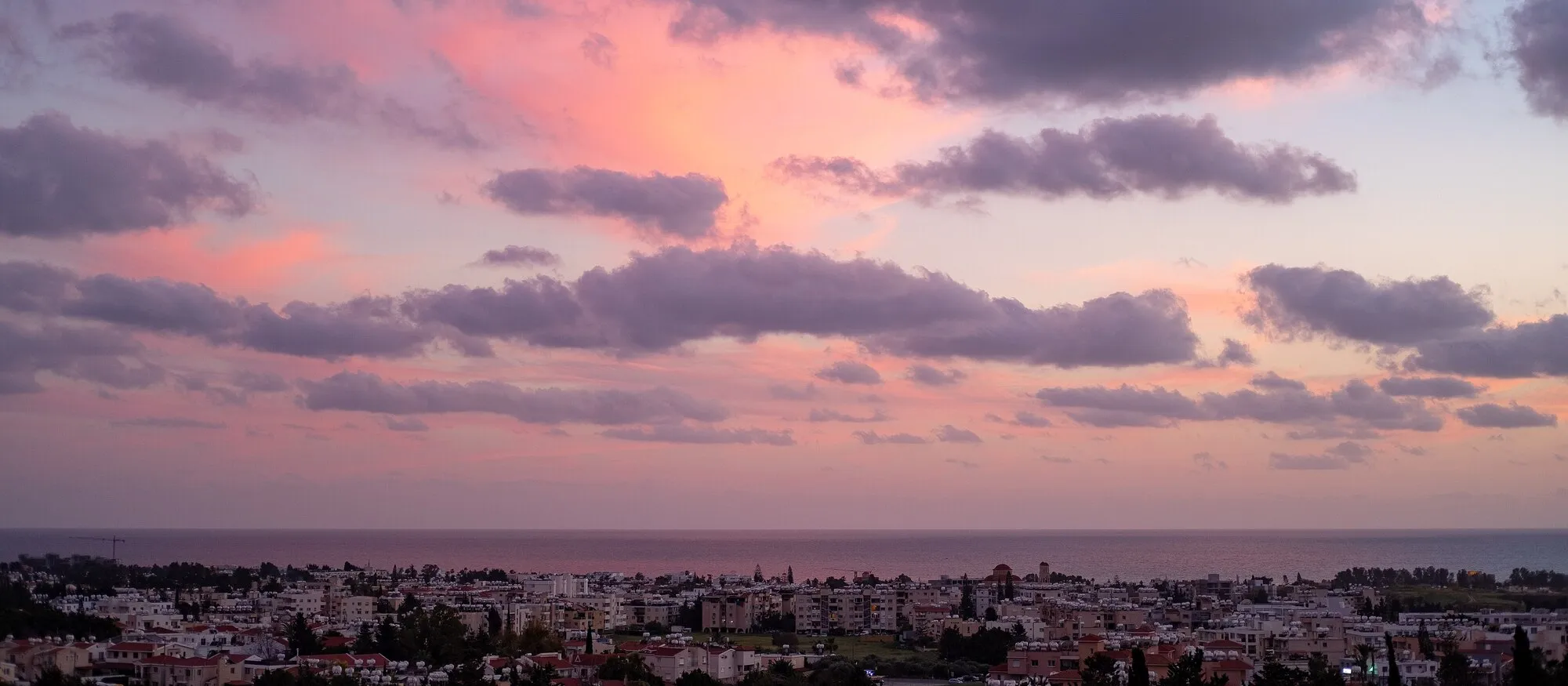Pink and violet sunset clouds over the rooftops of Paphos, with the Mediterranean on the horizon