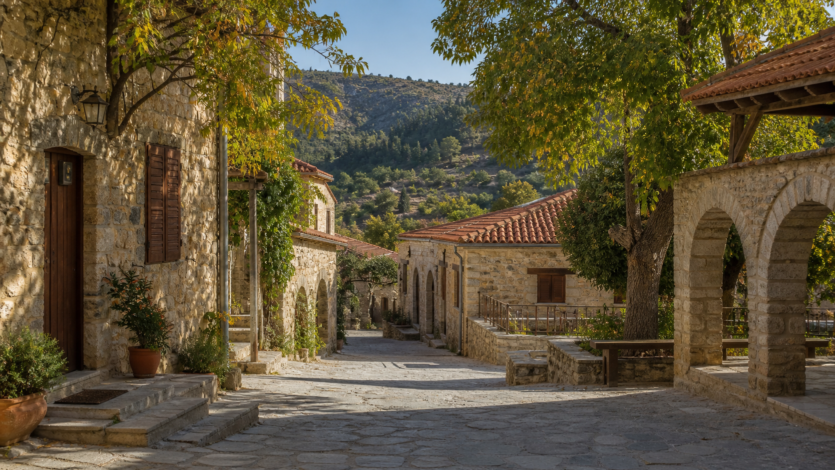 A quiet stone lane in a traditional Cyprus hillside village, with terracotta roofs and wooded hills beyond
