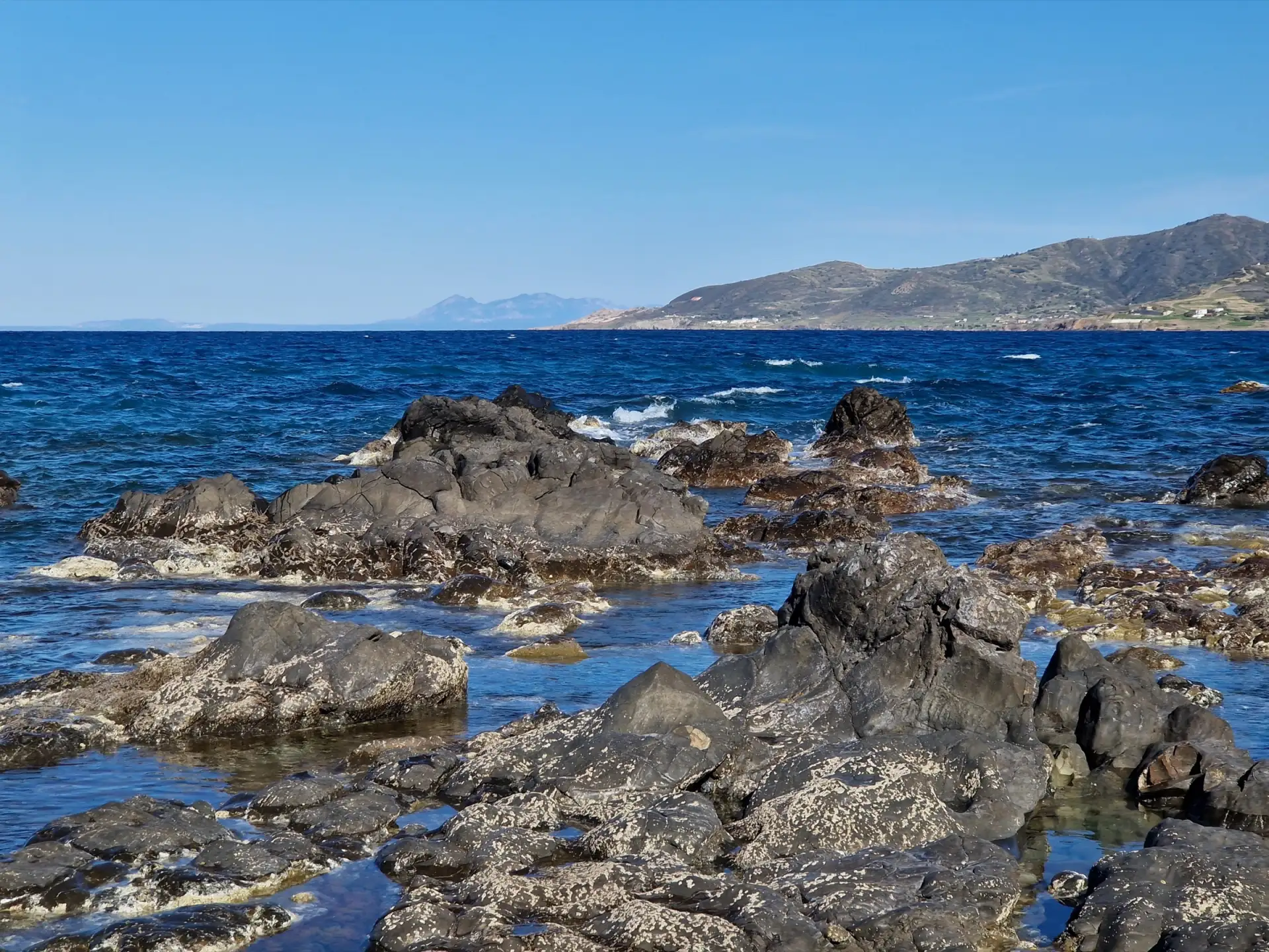 Clear blue sea and a rocky shoreline on the Cyprus coast near Pomos, with hills in the distance