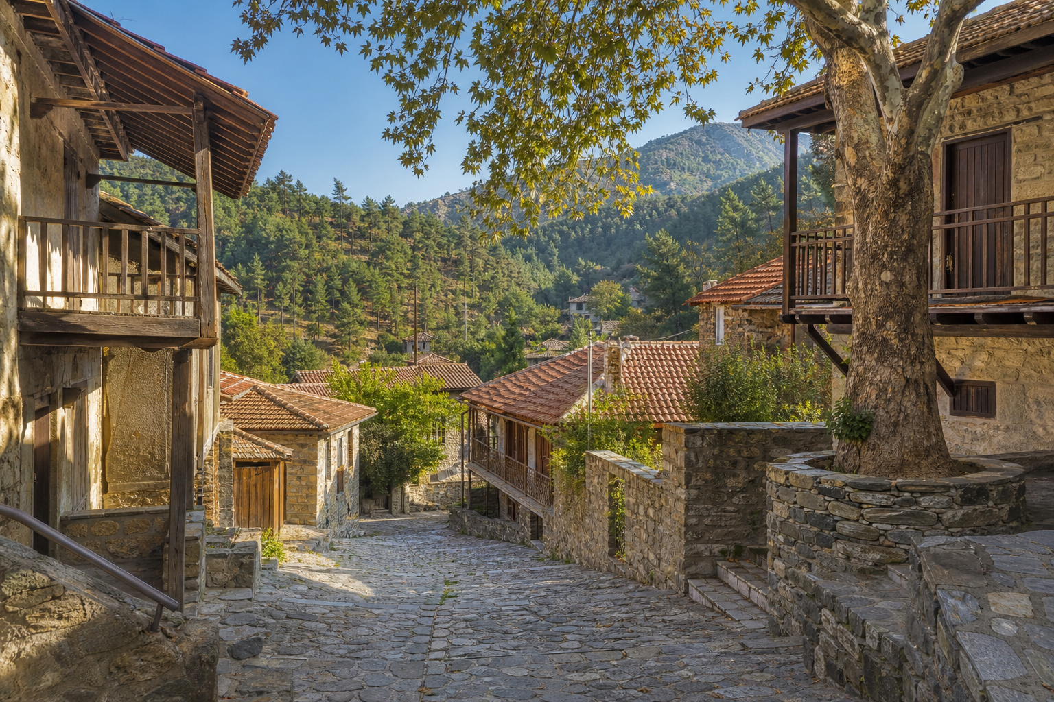 A stone-paved lane between traditional wooden-balcony houses in a Cyprus mountain village, with pine-covered Troodos hills behind