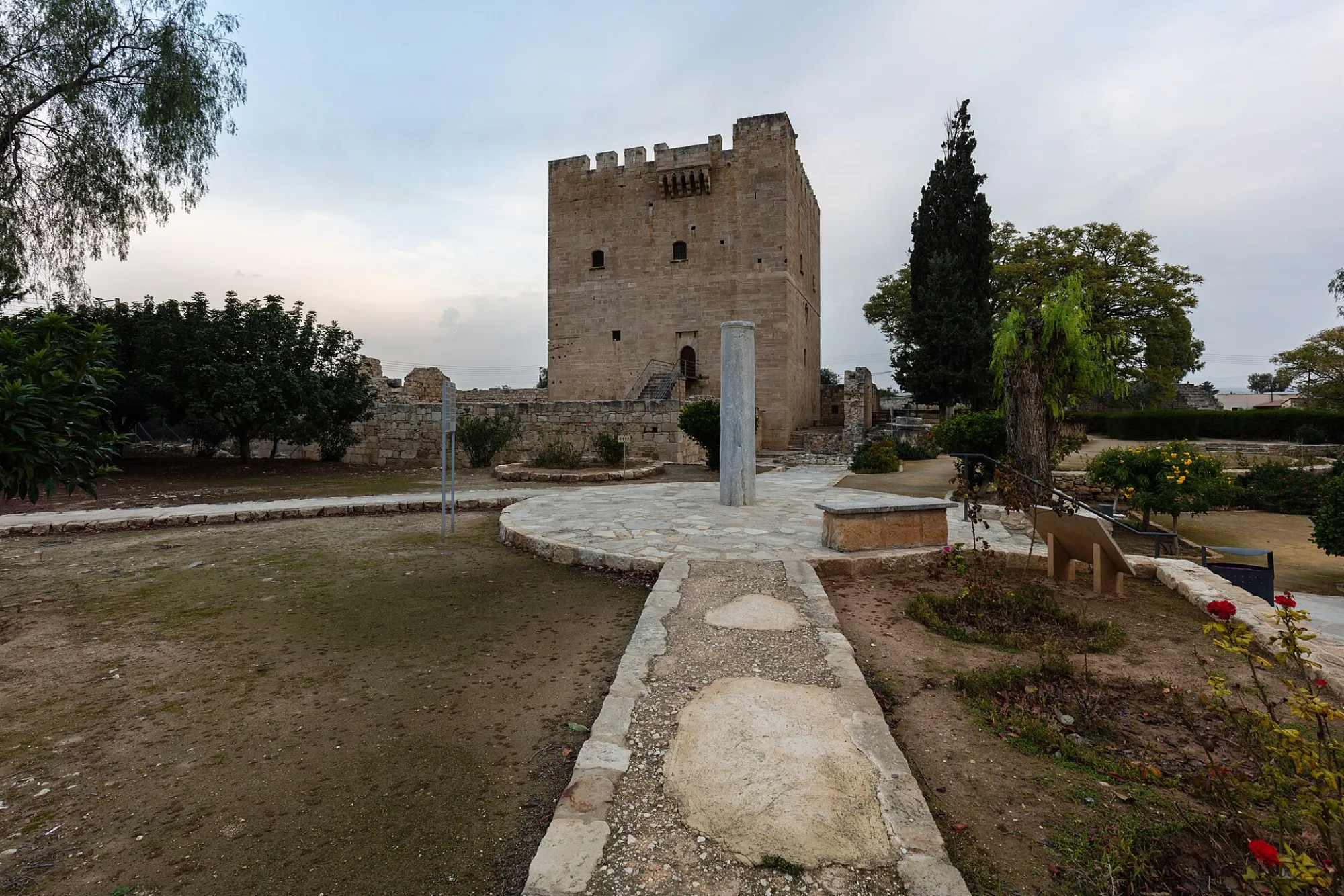 The square limestone keep of Kolossi Castle above its low enclosure walls and garden, with an external staircase to the raised entrance