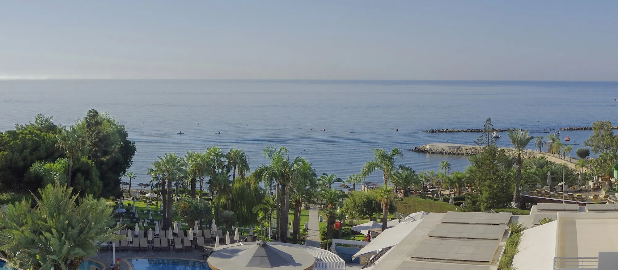 Palms, sunbeds and a rock breakwater along the hotel-strip coastline at Limassol, with calm sea beyond