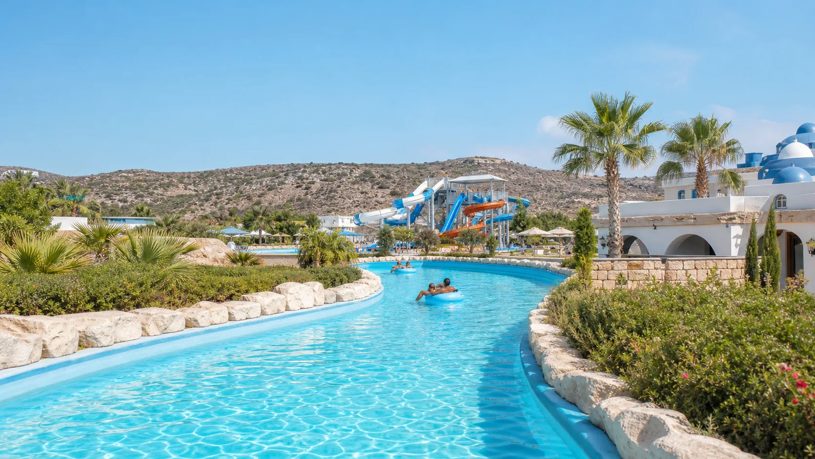 A turquoise lazy river winding past water slides and Mediterranean planting at a Cyprus water park