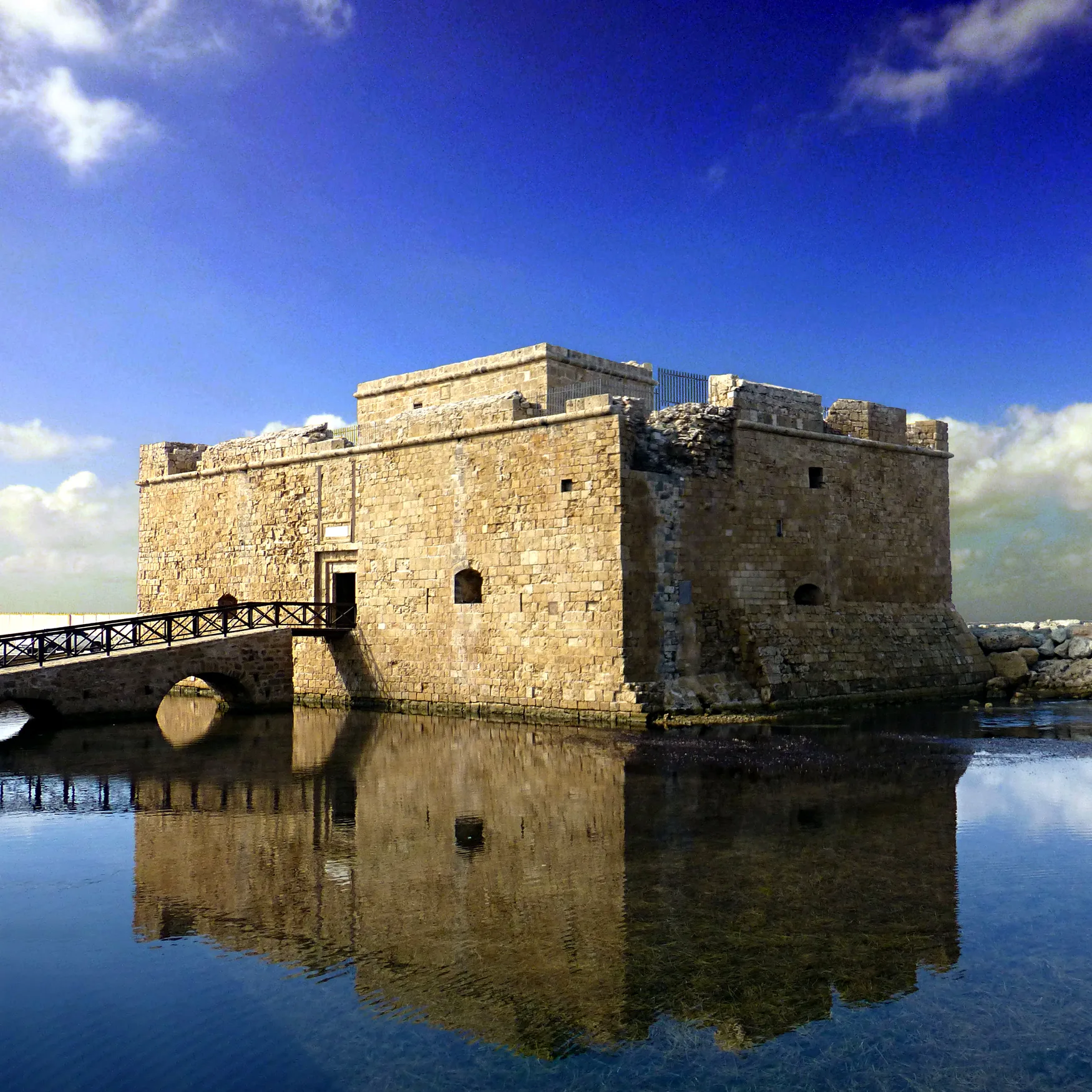 Paphos Castle, a square stone fort at the harbour edge, seen from the waterfront on a bright Mediterranean day