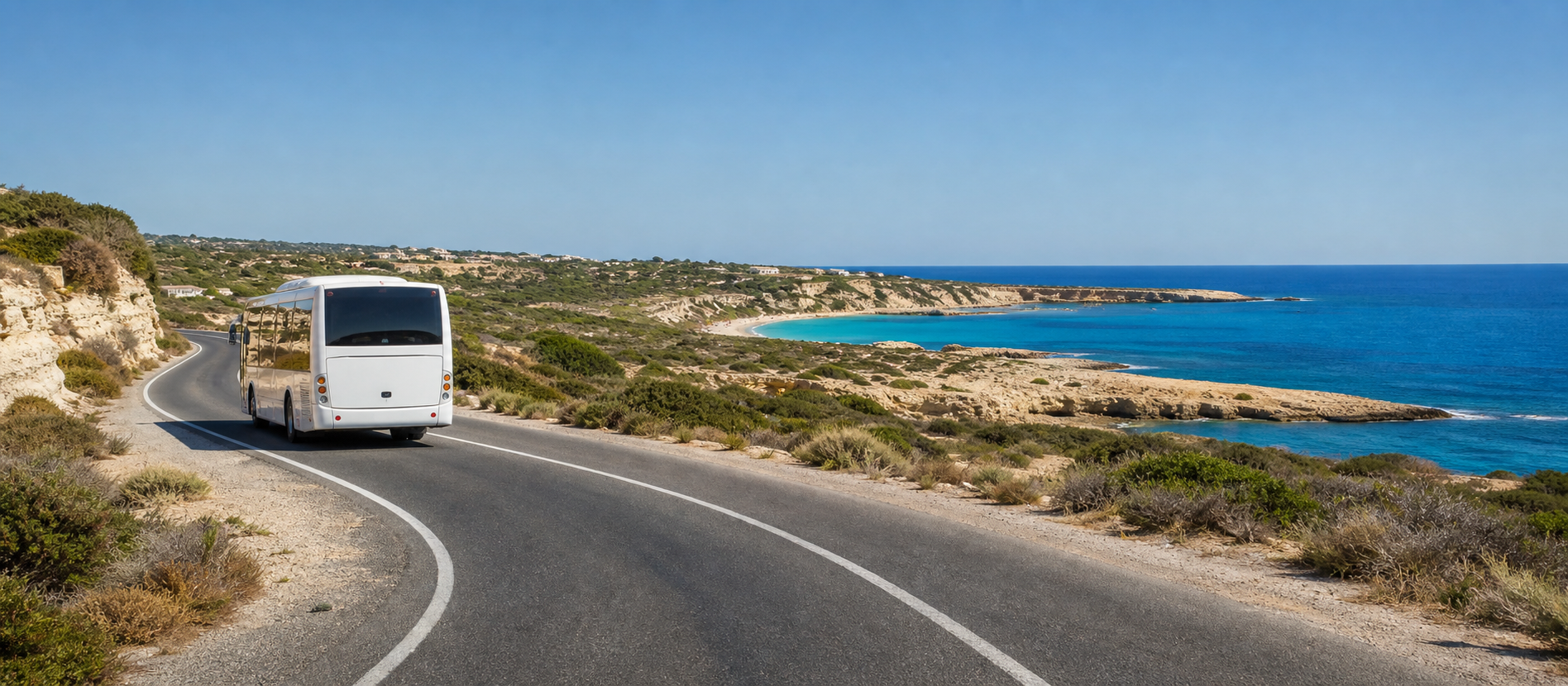 A white public bus on a coastal road above a turquoise bay near Paphos, Cyprus