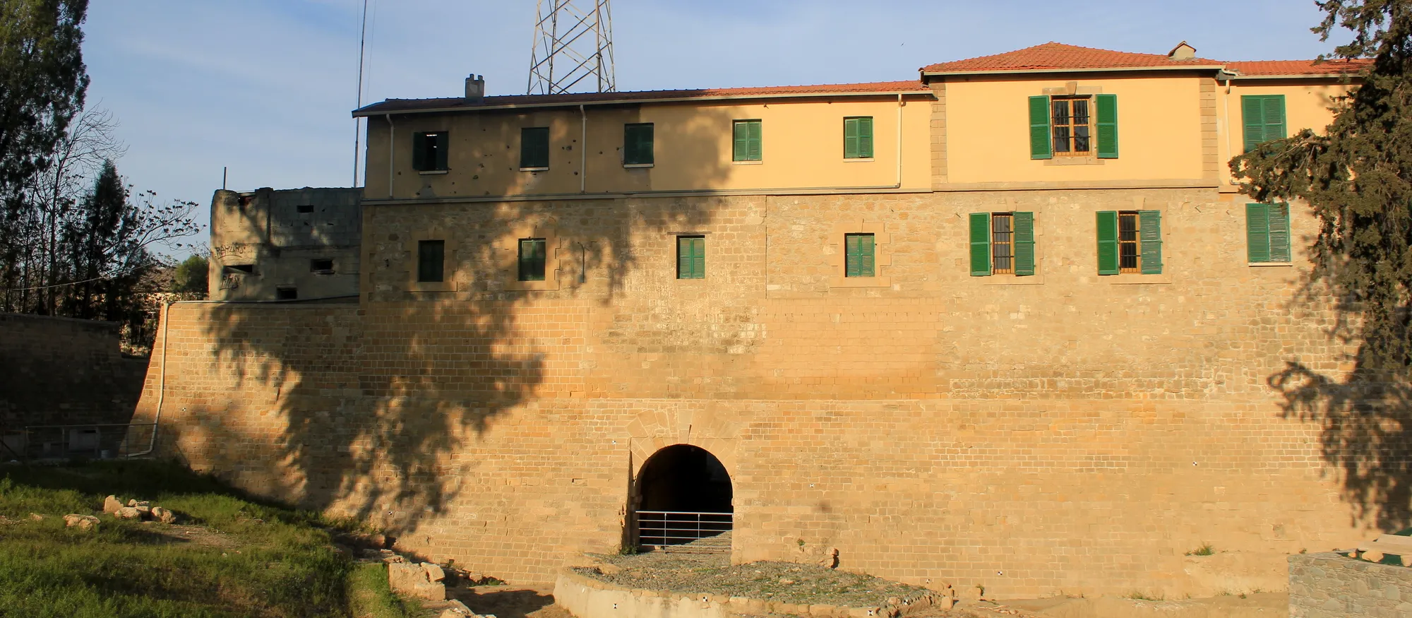 The Paphos Gate in Nicosia's Venetian walls in late-afternoon sun, a low arched tunnel in a sandstone wall with a two-storey building with green shutters on top