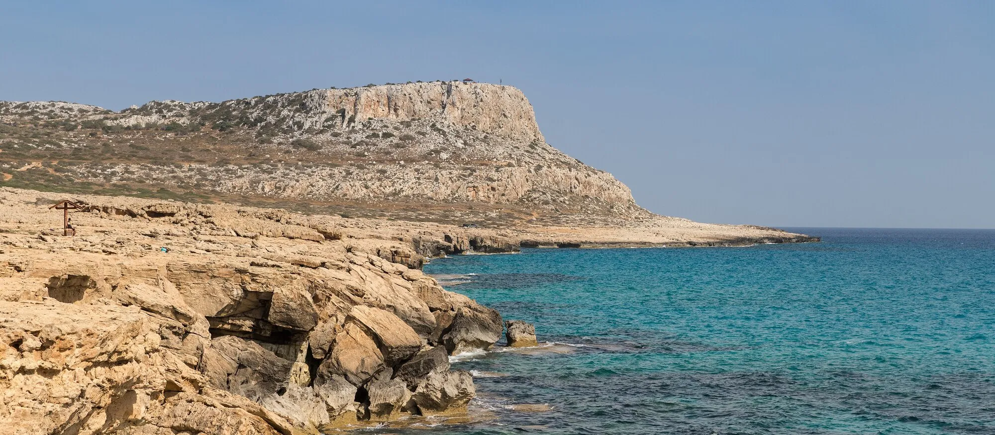 The flat-topped limestone headland of Cape Greco rising above pale rocky shore and turquoise sea, the protected cape that separates Ayia Napa from Protaras