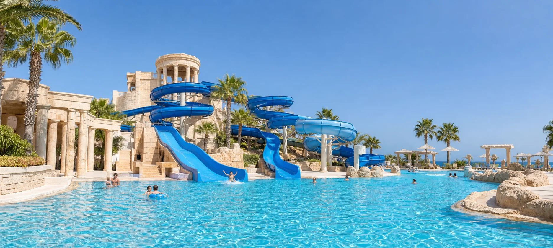 Blue water slides and a turquoise pool in a sunlit Mediterranean water-park setting